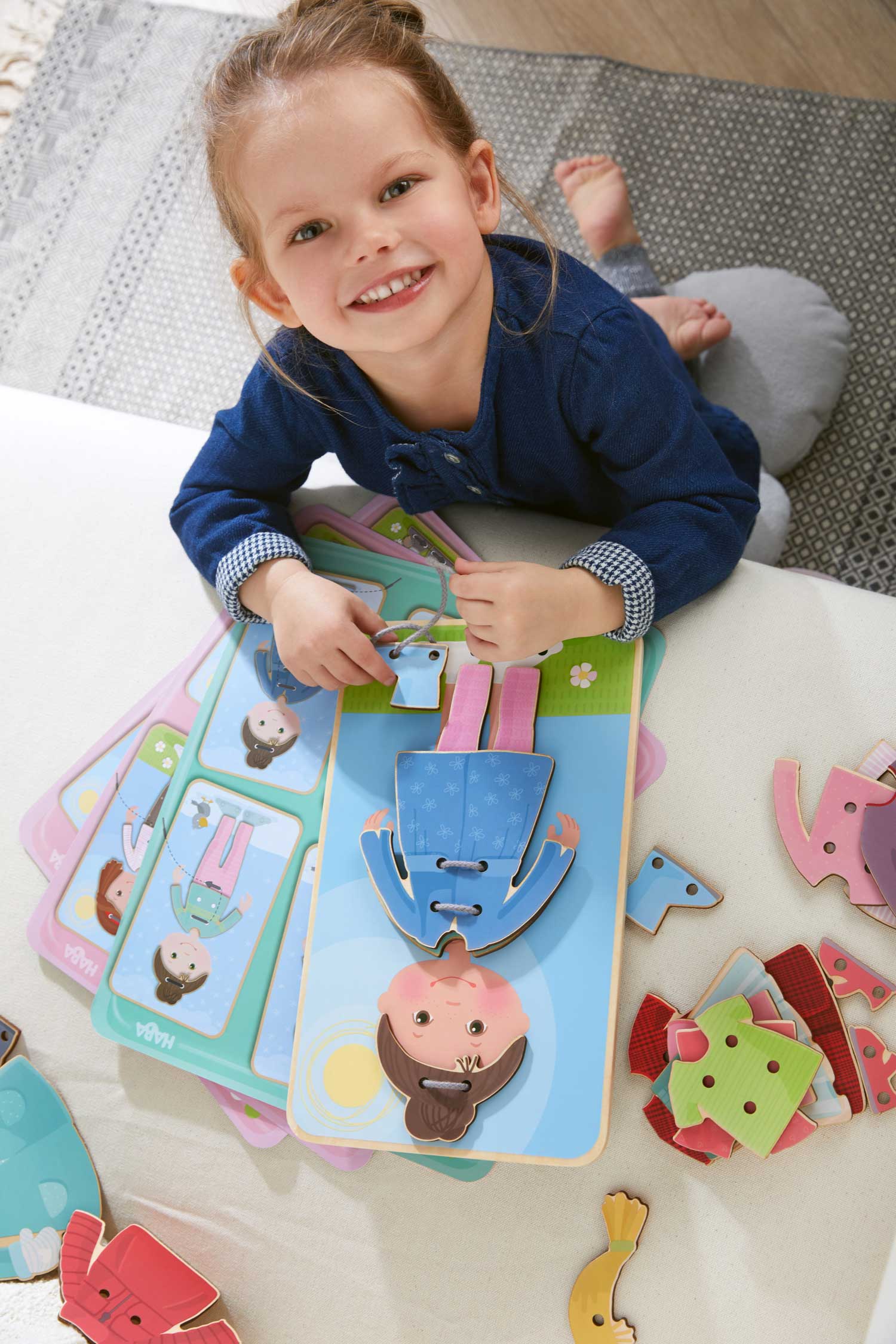 Child playing with a colorful dress up book and puzzle on a carpeted floor.